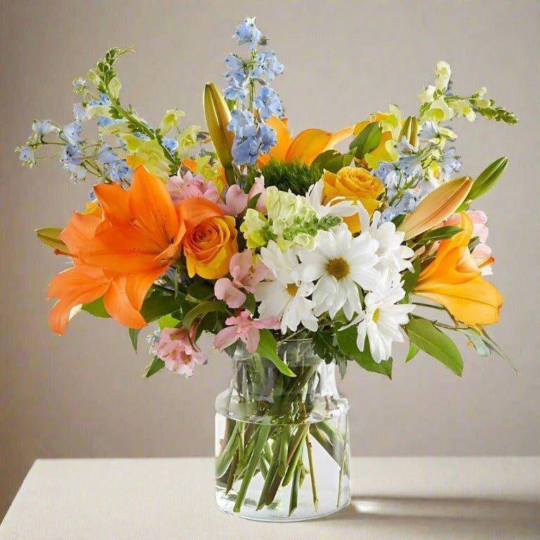 Large size of an orange blue and white floral arrangement in a clear vase.