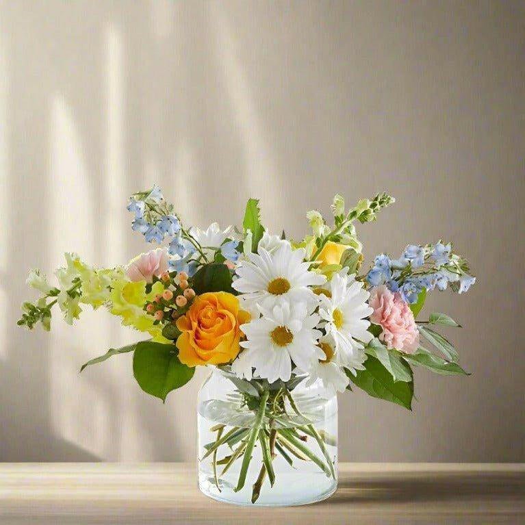 Small size of an orange blue and white floral arrangement in a clear vase.