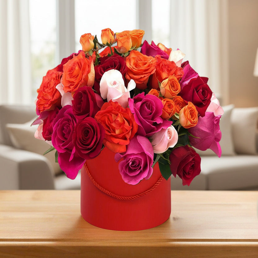 Mixed color roses in a red hat box with fillers and greens.