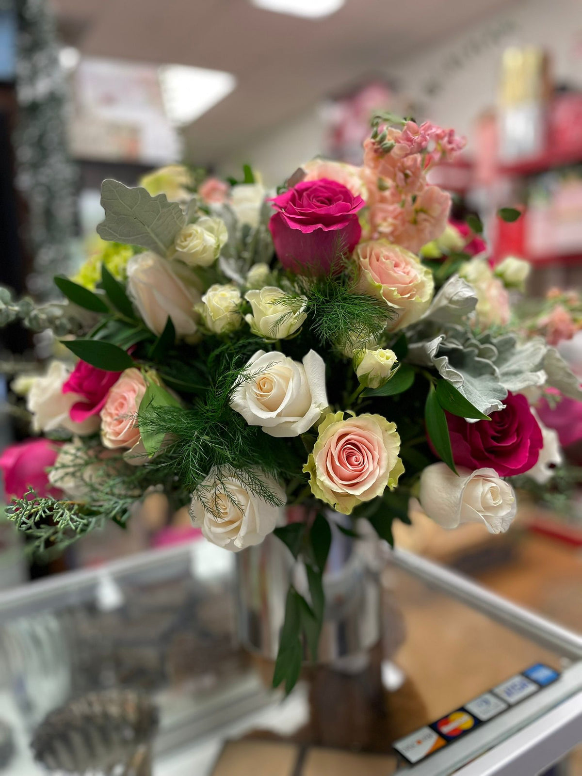 Colorful mixed roses arrangement with eucalyptus, and extra greens designed in a silver vase.