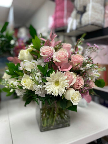 Floral arrangement in a clear square vase with white Gerbsers ponk roses stock flowers and green leaf's. 