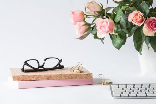 A office desk sowing a floral bouquet surrounded with books and a keyboard. 