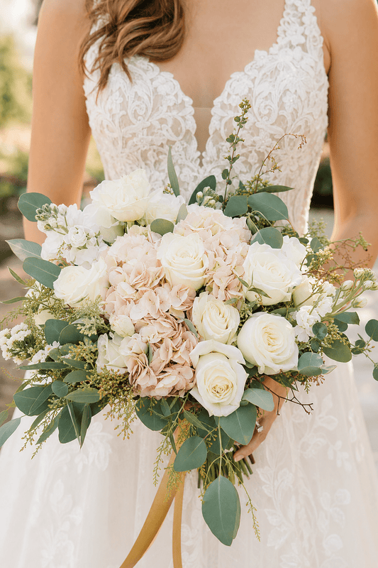 A photorealistic close-up of a bride holding a lush bridal bouquet of white roses, blush hydrangeas, and eucalyptus, with soft natural light. Alt: Blush and white wedding bouquet from Flower Shop in Hollywood