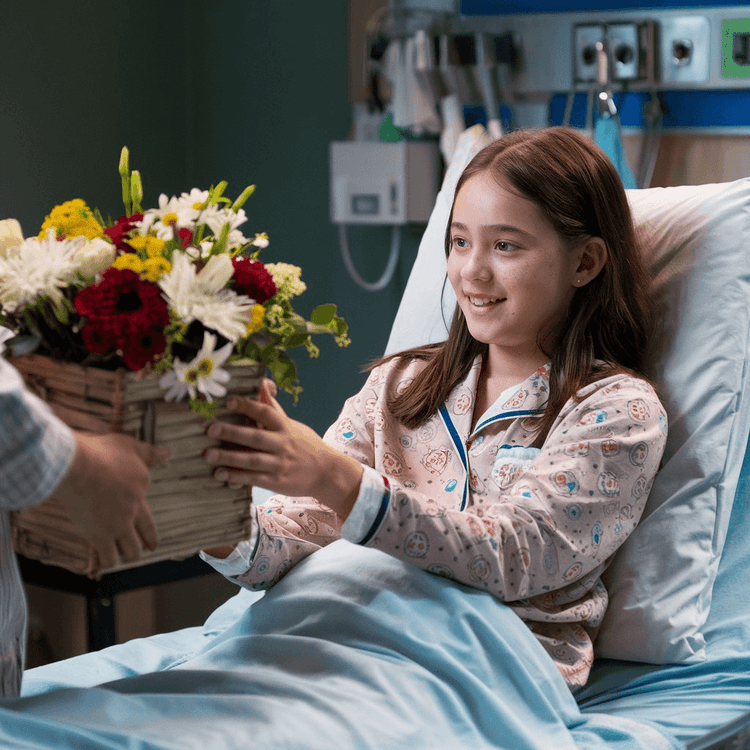 A girl lying in a hospital bed receiving a bright Get Well Flowers arrangement from Flower Shop in Hollywood.