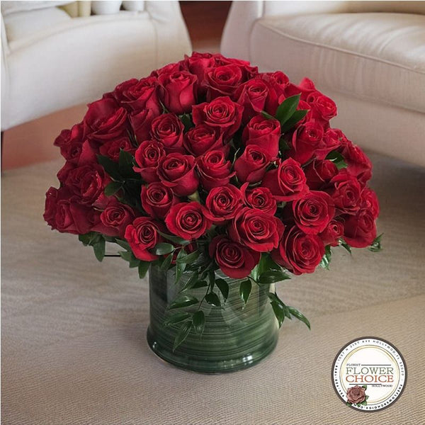 A large bouquet of red roses in a green vase, placed on a light-colored surface with a logo in the corner saying 'Flower Choice'.