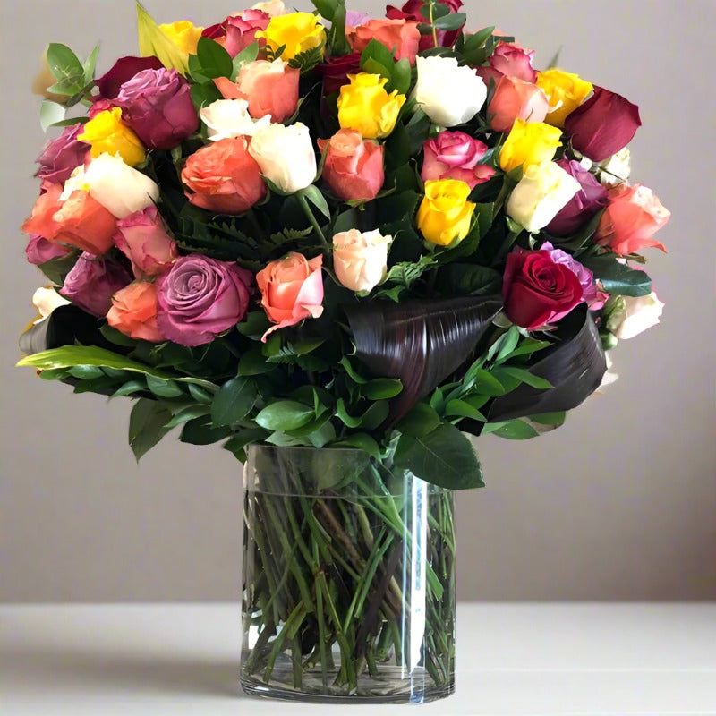 A bouquet of various colorful roses in a clear glass vase.