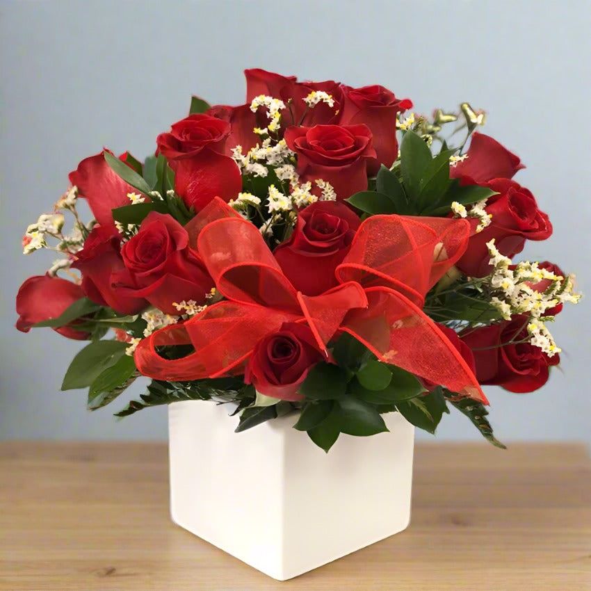 Bouquet of red roses with a red ribbon in a white vase.