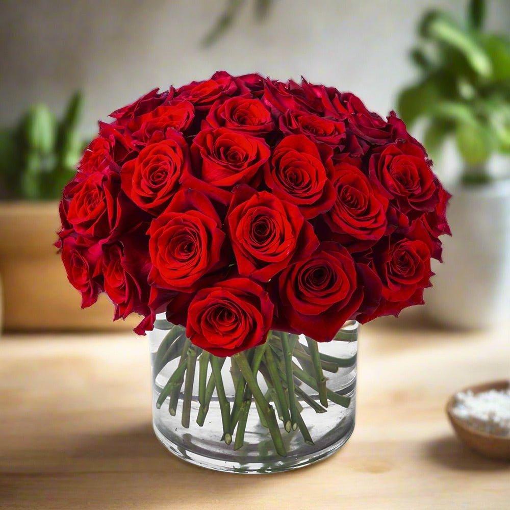 A bouquet of red roses in a clear glass vase on a wooden surface.