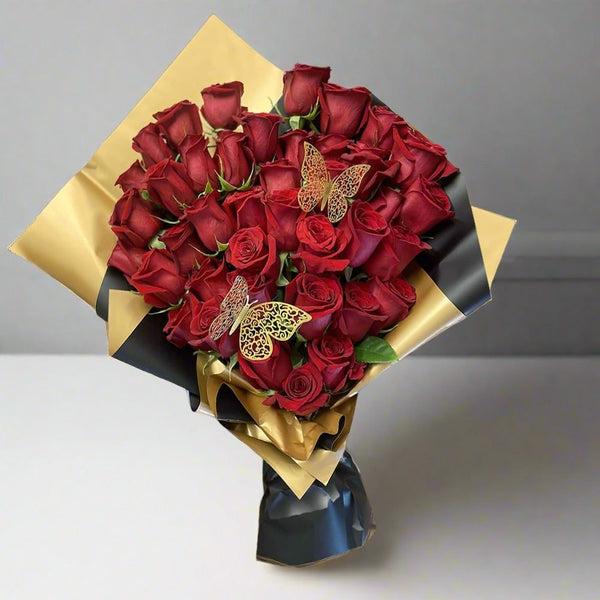 A bouquet of red roses wrapped in black and gold paper adorned with decorative gold butterflies.