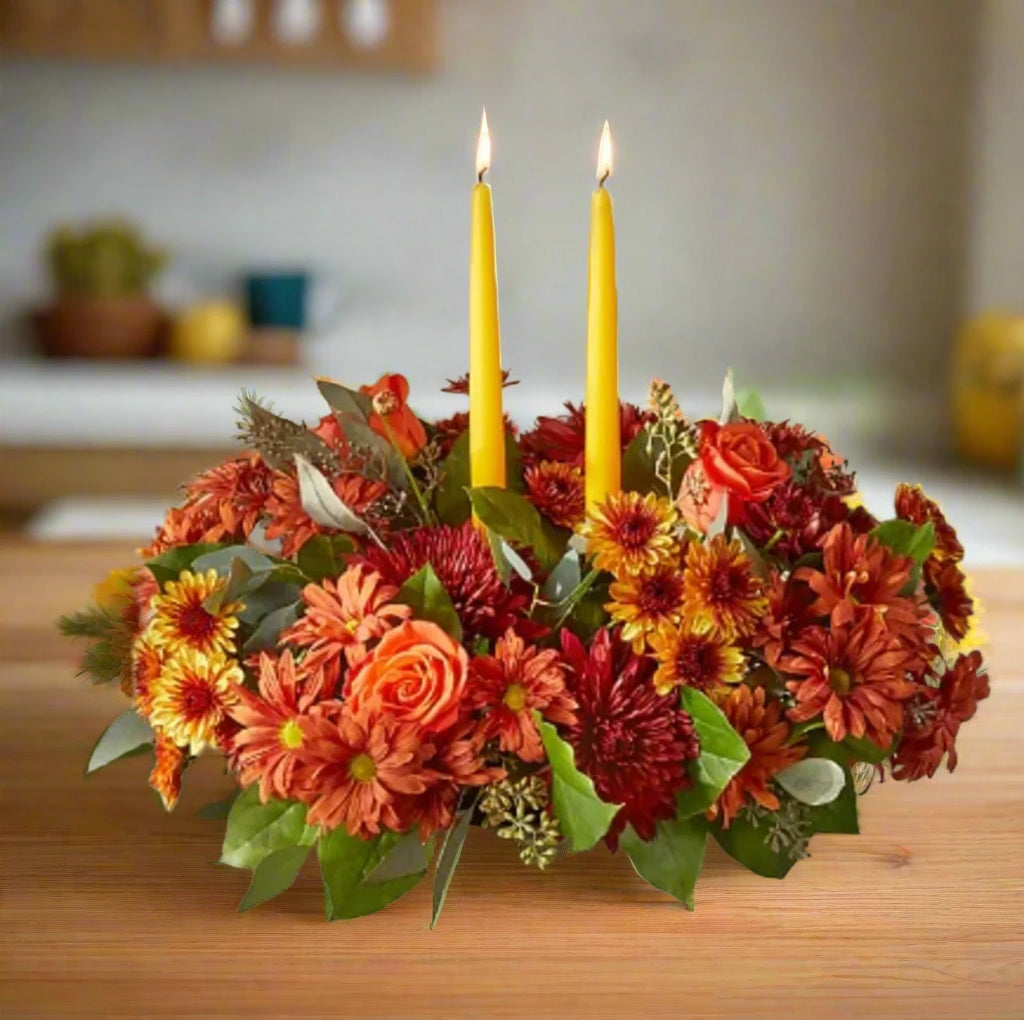 A fall color center piece with two yellow candles arranged in a table.