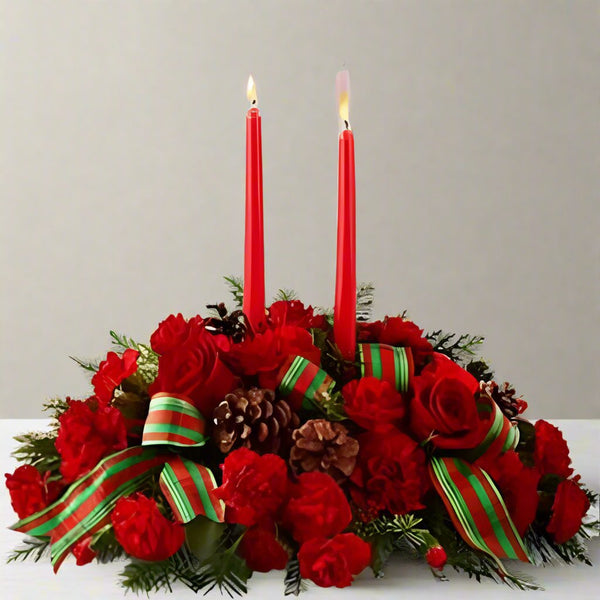 Holiday Classics Centerpiece with two candles with roses and carnations and a red and green ribbon with Christmas greens.