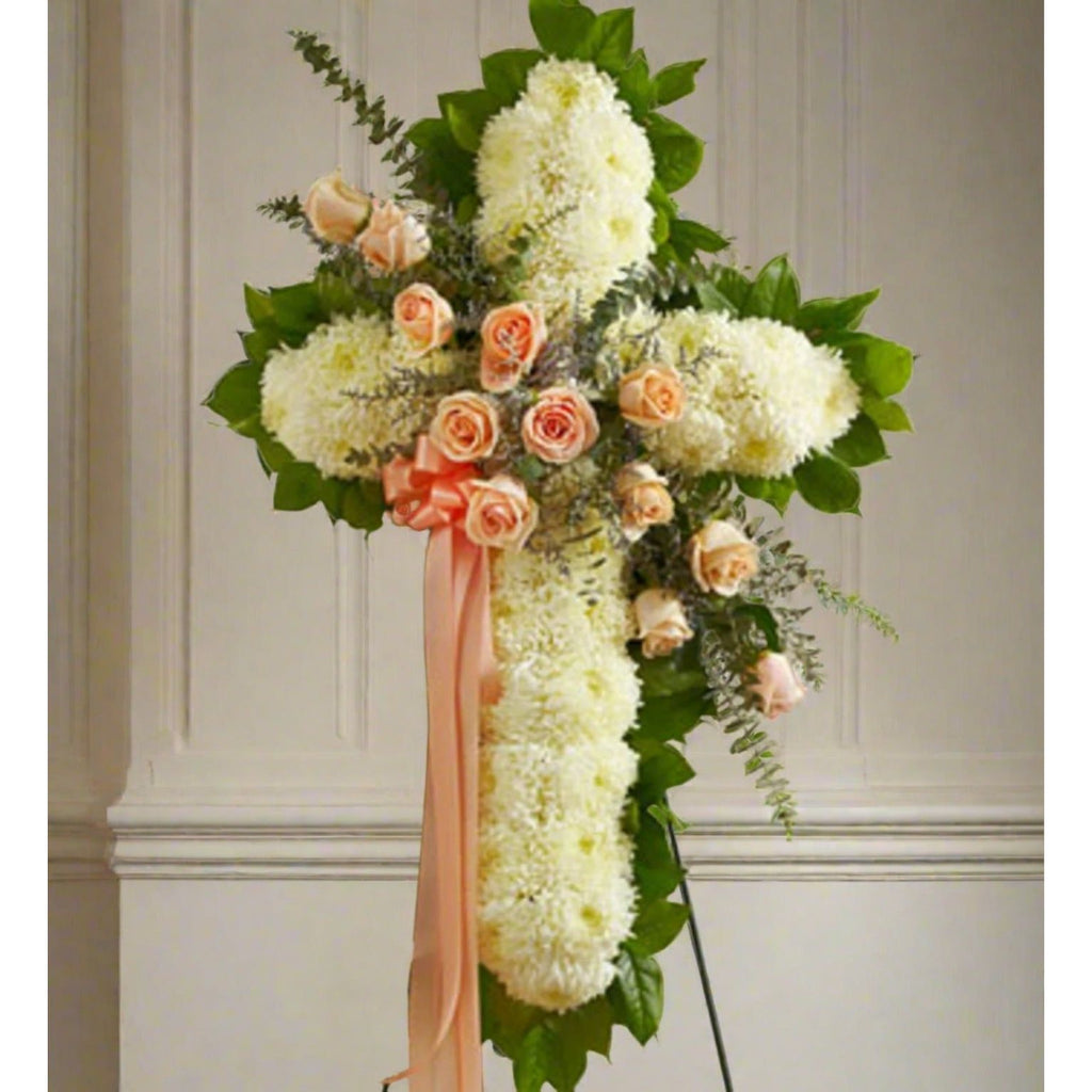 White standing cross with peach roses across with a peach ribbon on the side