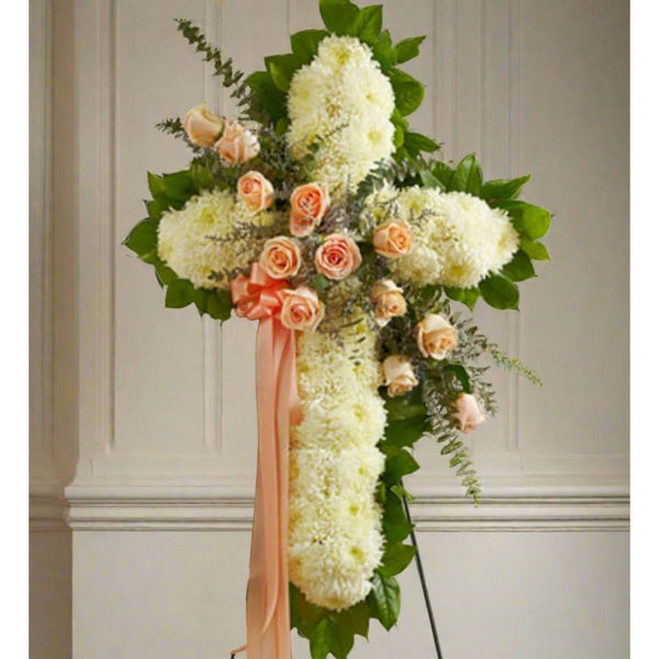 White standing cross with peach roses across with a peach ribbon on the side