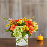 fall floral arrangement in a clear vase with orange, yellow, red and green flowers.