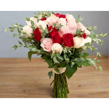 Bouquet of red and white roses with green leaves on a wooden surface.