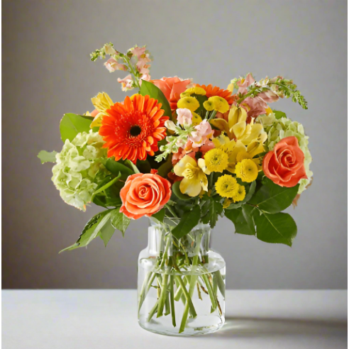 A bouquet of diverse colorful flowers including roses and daisies in a clear glass vase.