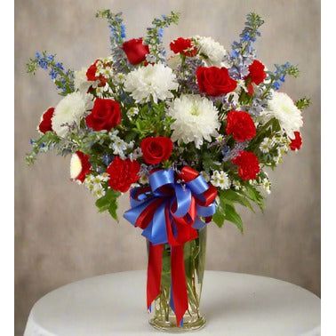 A bouquet of red, white, and blue flowers in a vase with red and blue ribbons.