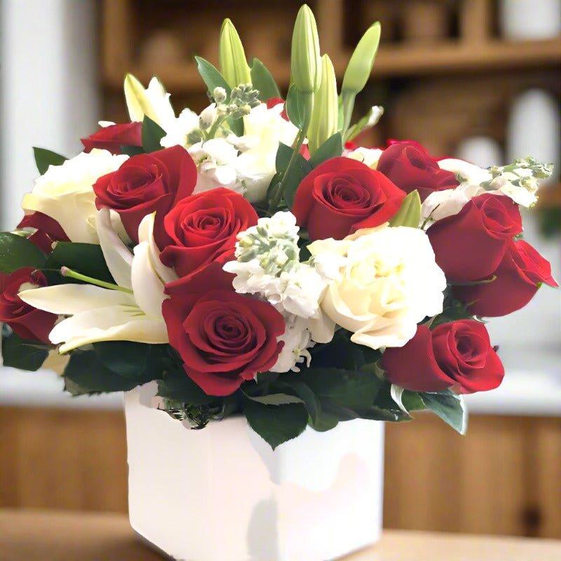 A bouquet of red and white roses with green leaves in a white vase.