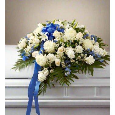 Blue white casket spray cover set on a casket with white roses and blue ribbon on the side.