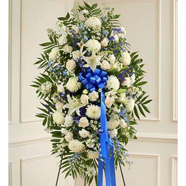 Blue & White Standing Spray with white roses, pomp's and greens with a blue ribbon on the side.