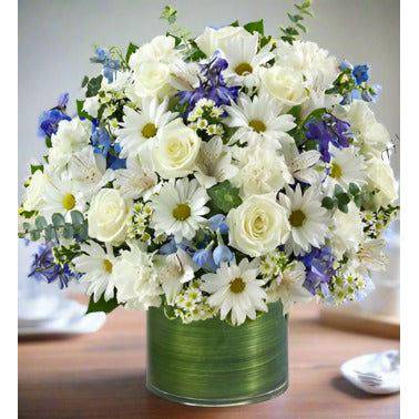 This stunning Blue and White Tribute floral Arrangement of blue and white roses in a clear vase with fillers and greens