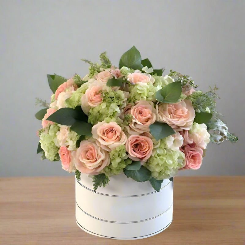 Bouquet of pink and green flowers in a white round box on a wooden table.