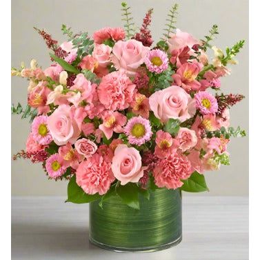 A bouquet of pink roses, carnations, and other flowers in a green vase.