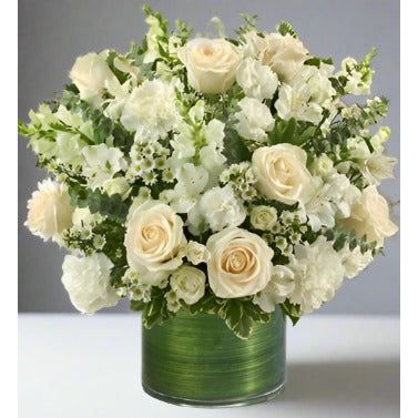 All white mix flowers with roses, carnations, hydrangeas set in a clear cylinder vase with greens