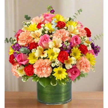 A vibrant bouquet of various flowers including roses, carnations, and daisies in a green vase.