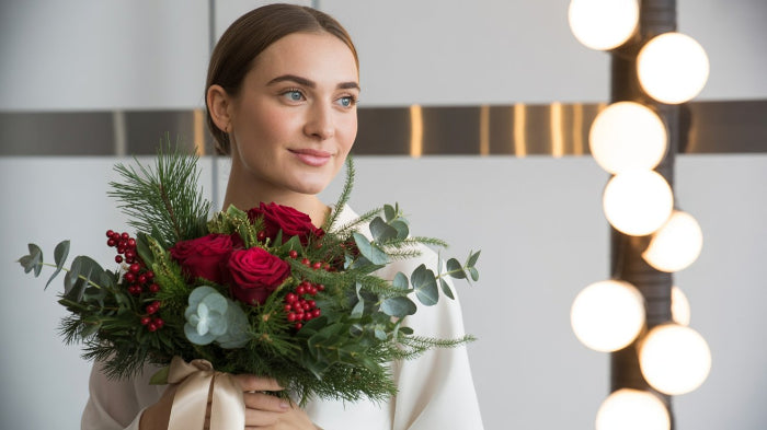 Woman holding a bouquet of red roses and greenery in front of a softly lit background