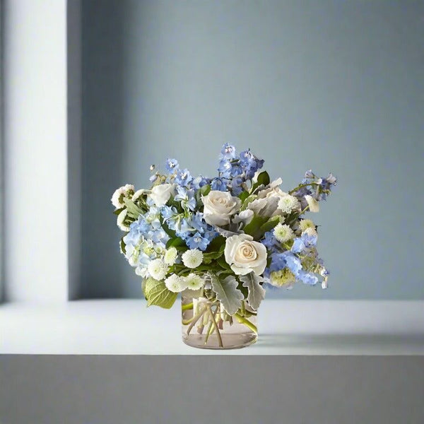 Bouquet in a glass vase featuring white roses and blue flowers.