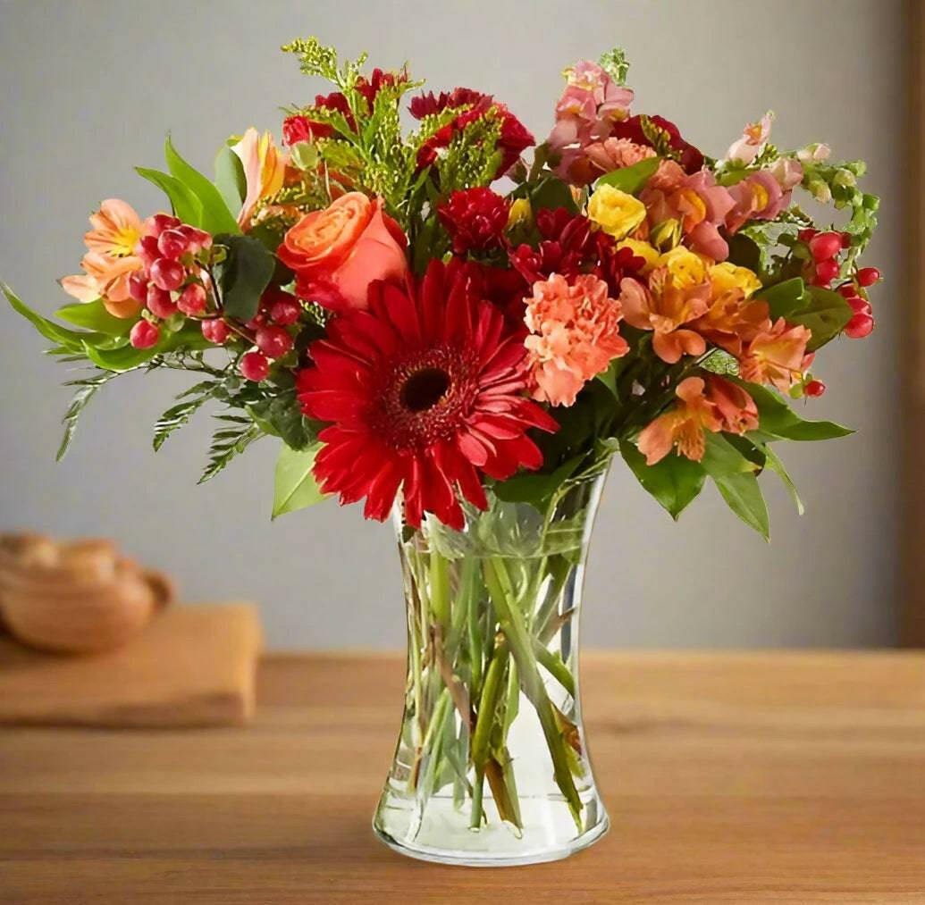 Fall floral arrangement with orange roses carnations, and Gerber's in a medium clear vase