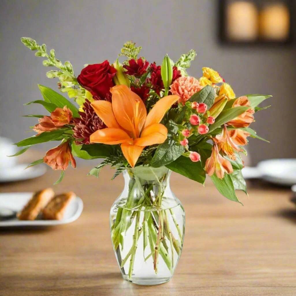 Fall floral arrangement of orange lilies and red roses in a small clear vase