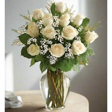 Bouquet of white roses with greenery in a clear glass vase.