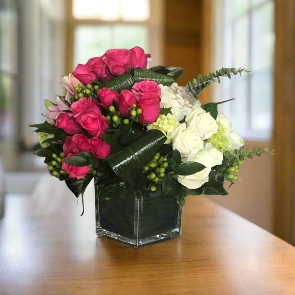 A bouquet of pink and white flowers in a glass vase on a wooden table.