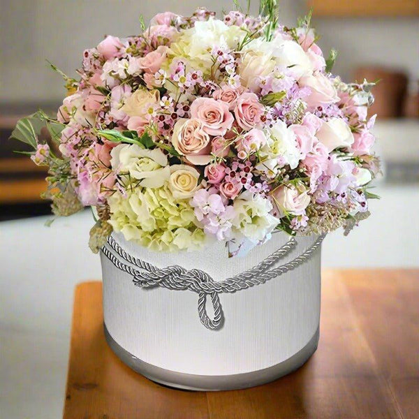 Elegant flower arrangement in a white decorative round box on a wooden table