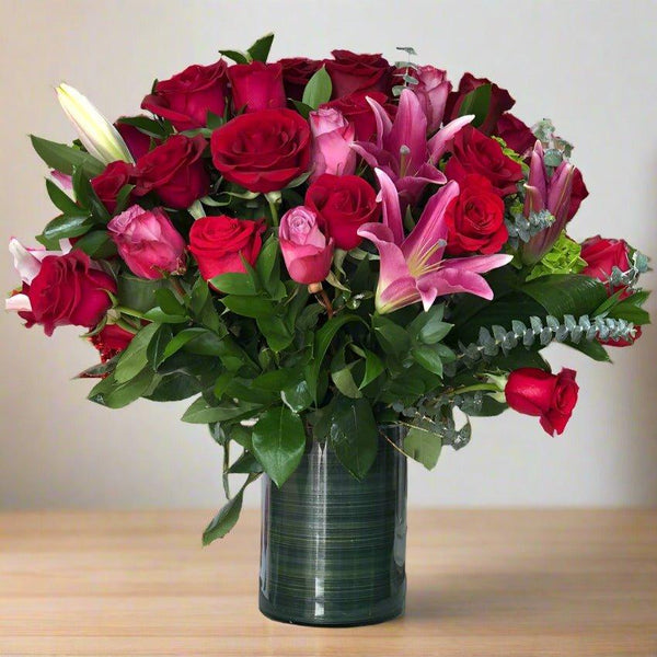 Bouquet of red roses and pink lilies in a clear vase.