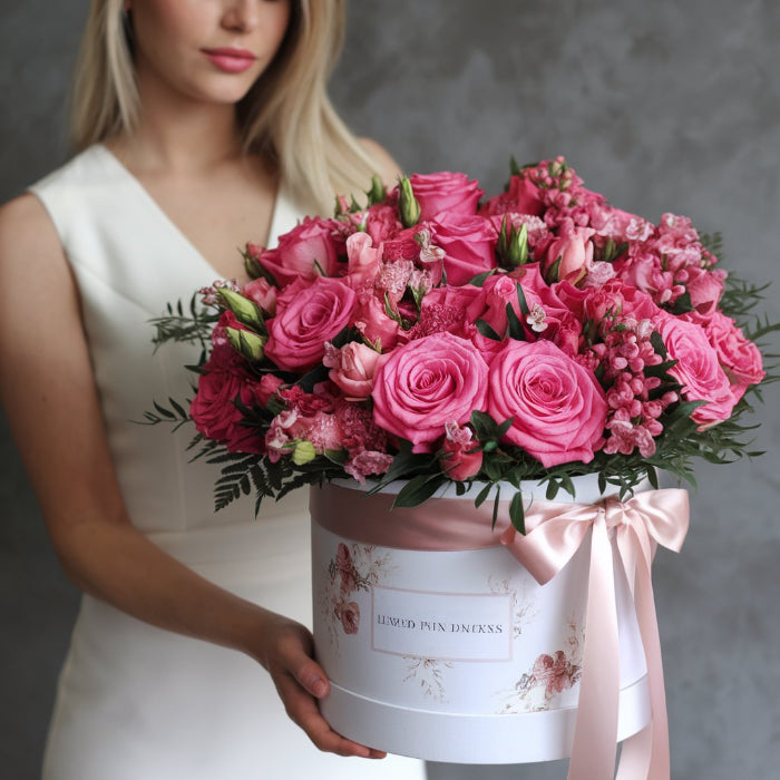 Woman holding a bouquet of pink flowers in a decorative box with a bow.