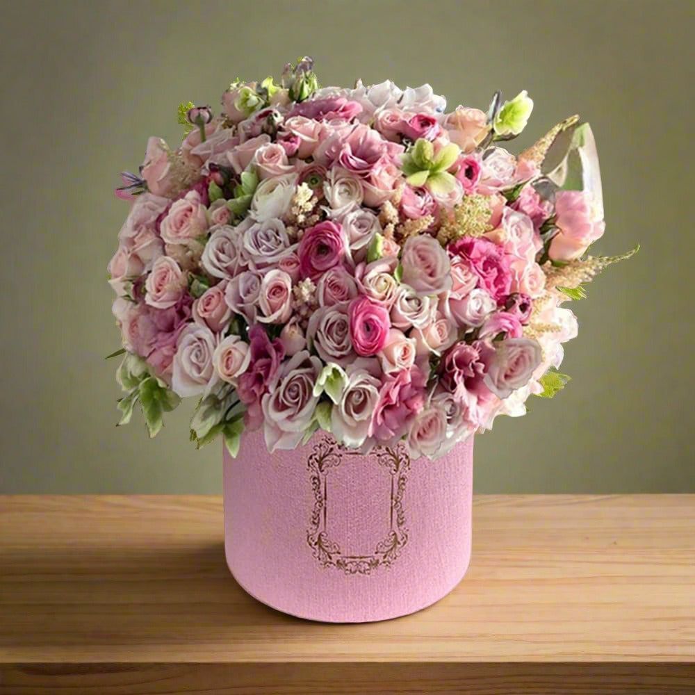 A bouquet of pink and white roses in a decorative pink round box placed on a wooden table.