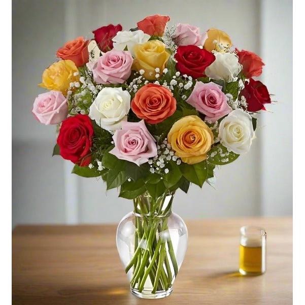 Bouquet of roses with various colors in a clear glass vase on a wooden table.