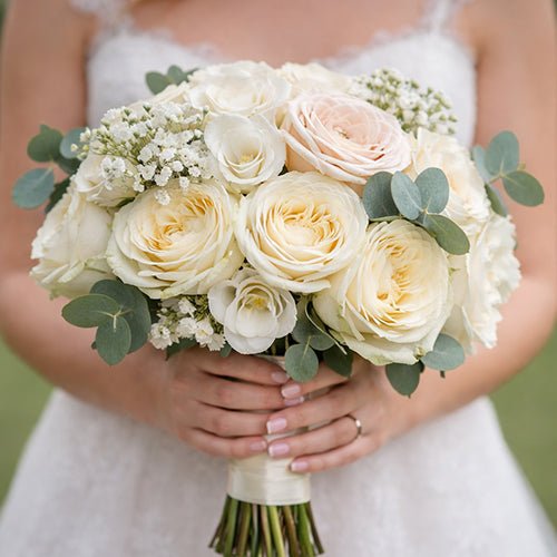 Bouquet of white and light pink roses held by a person in a white dress.