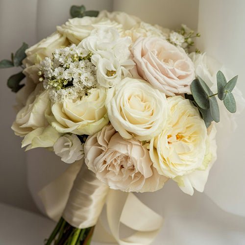 Bouquet of white and light pink roses with greenery on a neutral background