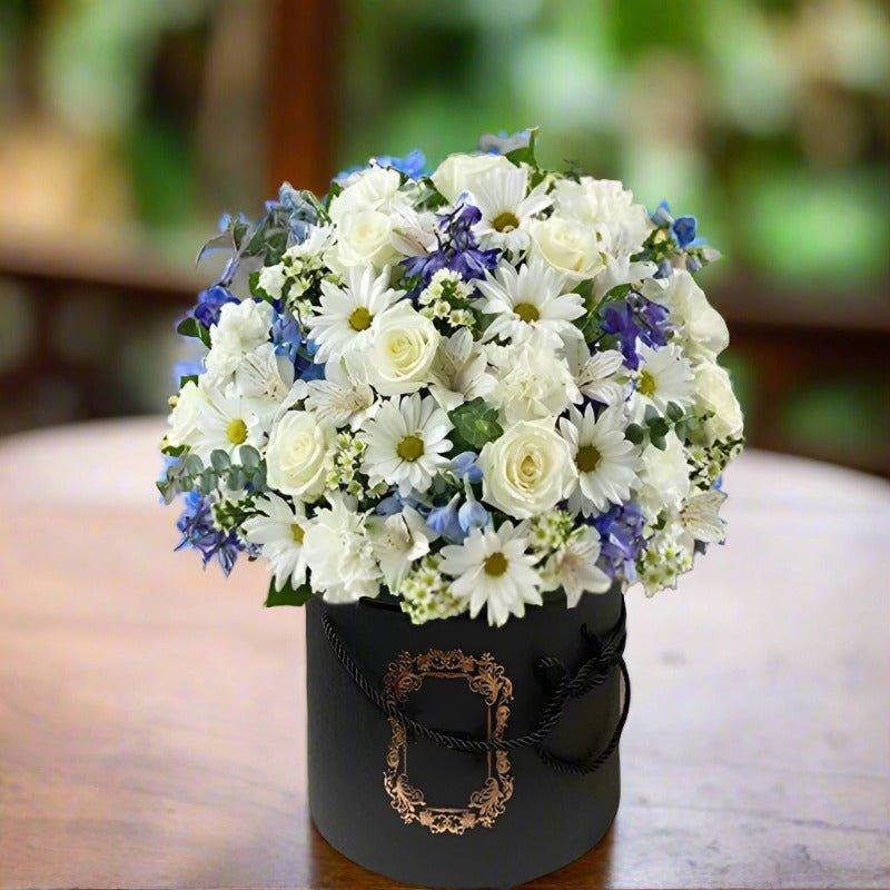 Bouquet of white and purple flowers in a decorative black box on a wooden table.