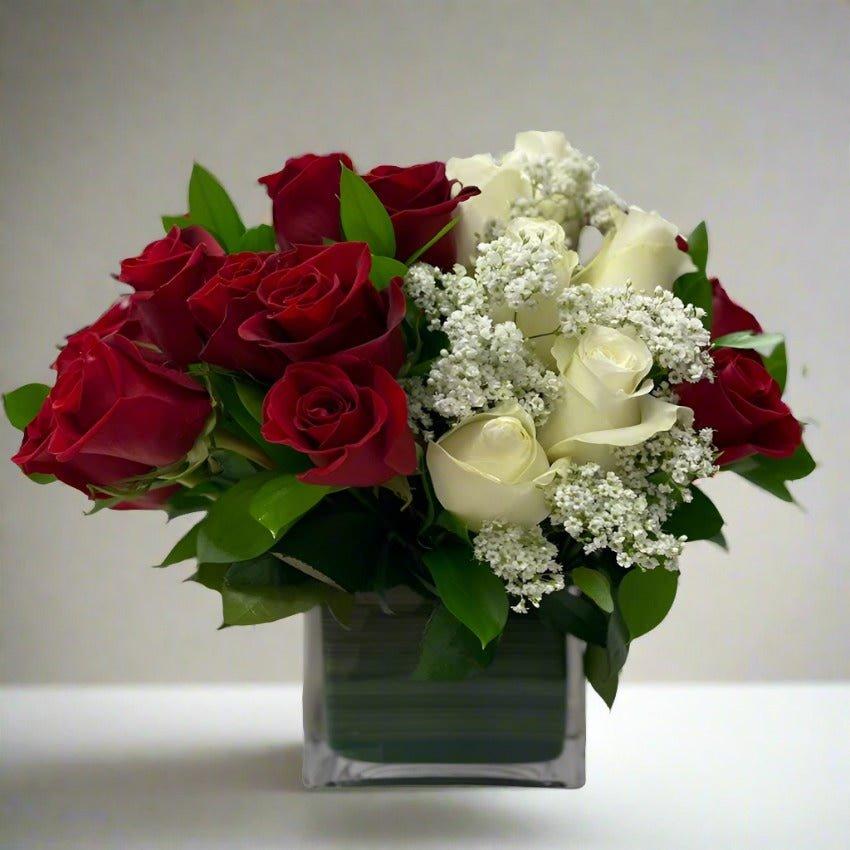 Bouquet of red and white roses with greenery in a square vase