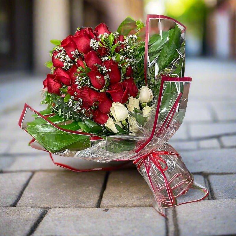 Bouquet of red and white roses wrapped in cellophane, placed on a paved pathway.