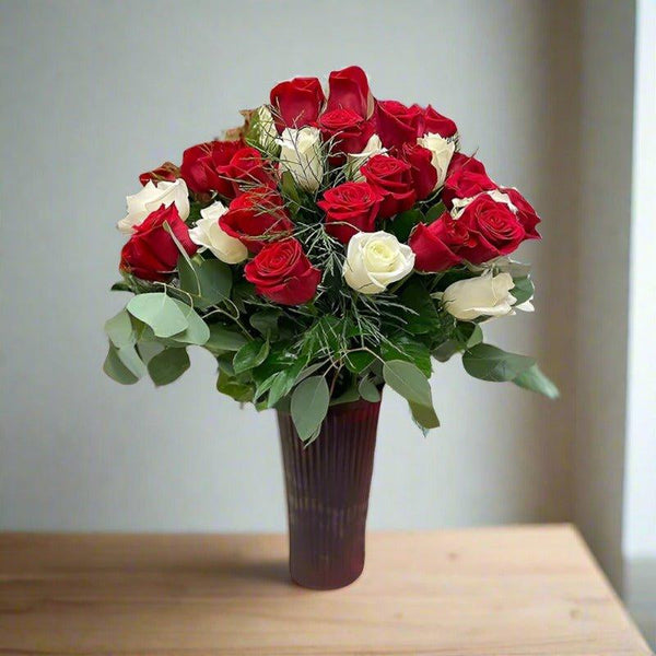 Red and white roses in a tall vase on a wooden table