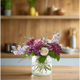 A vase of assorted colorful flowers on a wooden table in a kitchen.