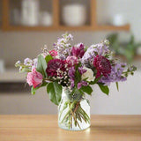 A bouquet of assorted flowers in a glass vase on a wooden table.