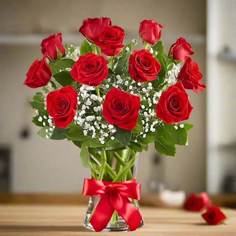 A bouquet of red roses in a clear glass vase tied with a red ribbon.