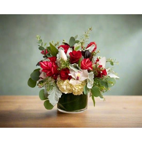 A floral arrangement with red, white, and cream flowers in a glass vase on a wooden table.